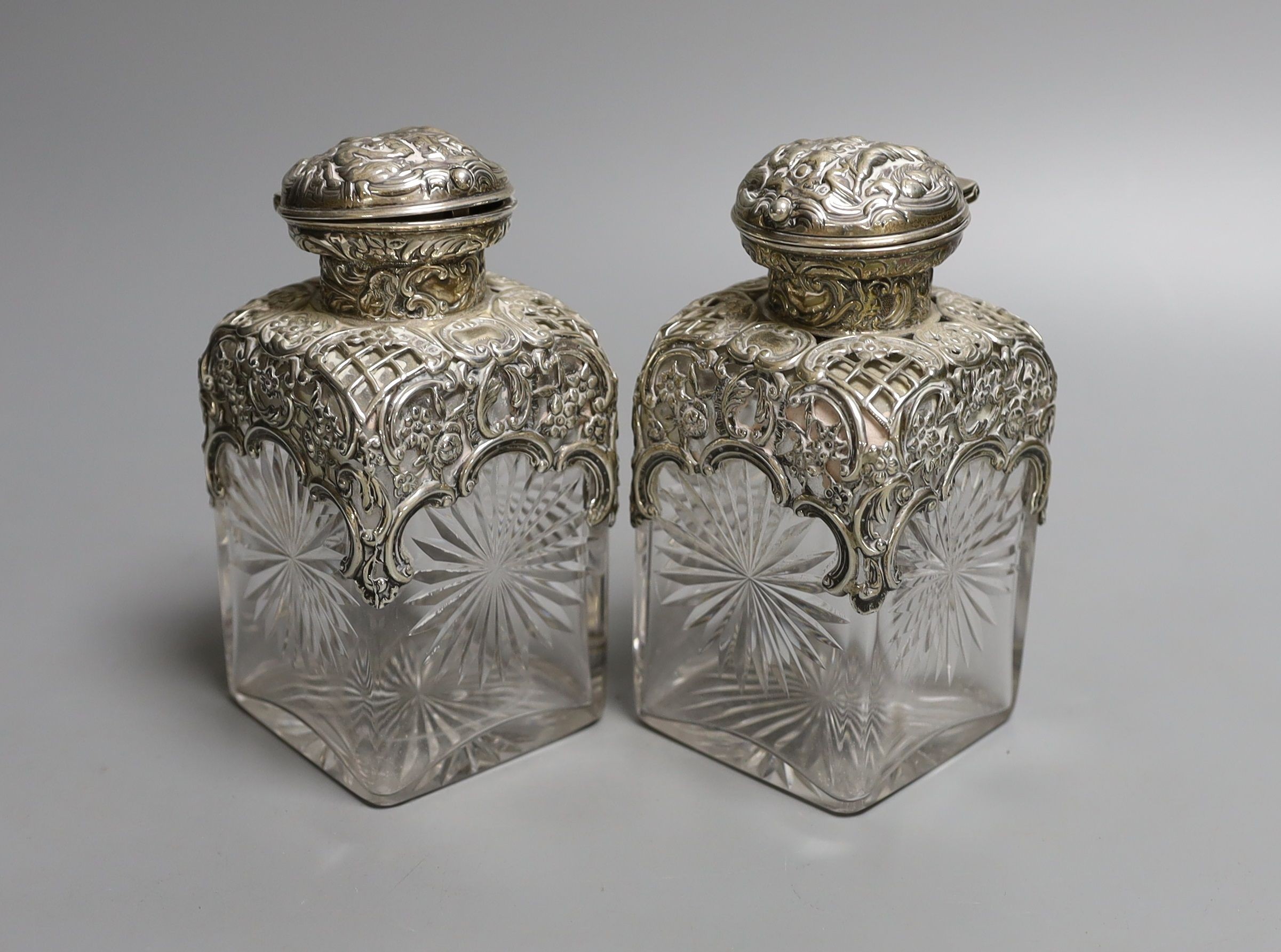 A pair of late Victorian repousse silver mounted cut glass scent bottles with stoppers, William Comyns, London, 1898, height 14.3cm.